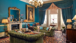 A room with a green sofa, a fireplace, a large mirror, and a chandelier.