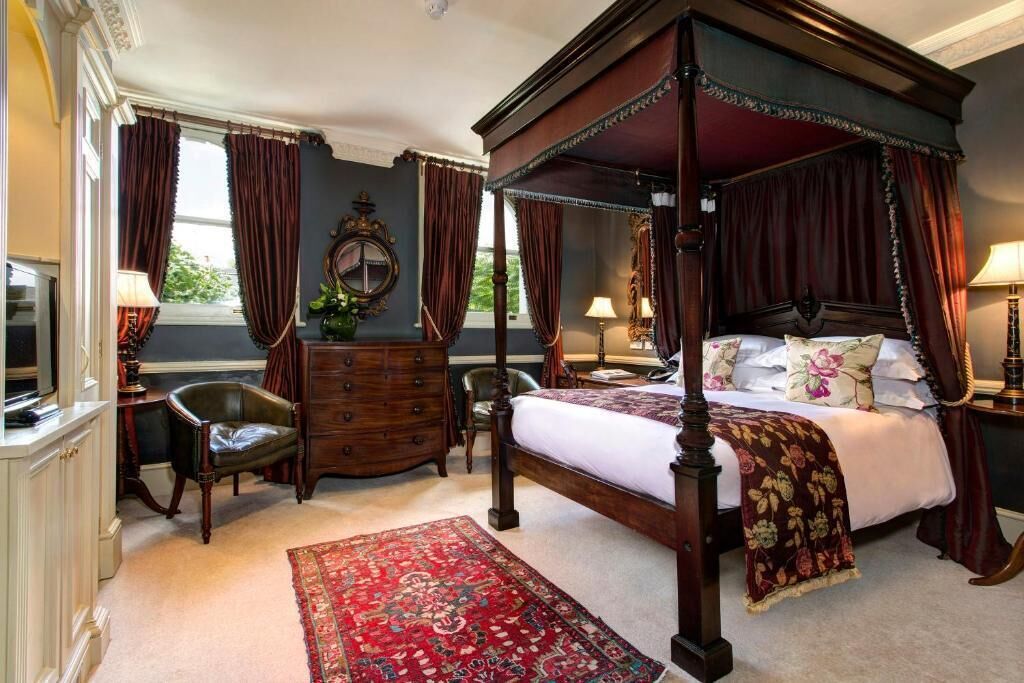 A four-poster canopy bed with a red and white bedspread, a wooden dresser, a red patterned rug, and a large mirror on the wall.