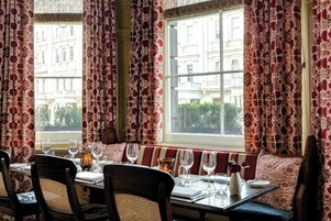 Un comedor con una mesa para cuatro, una banca y vistas a un edificio a través de cortinas estampadas.