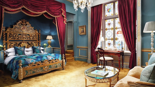 A luxurious bedroom with a large ornate bed, a glass coffee table, and a view of a cityscape through a window with stained glass. - The Gore London – Starhotels Collezione (London)