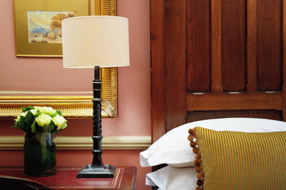 A hotel room with a wooden headboard, a bedside lamp, a vase with flowers, and a framed picture on the wall.