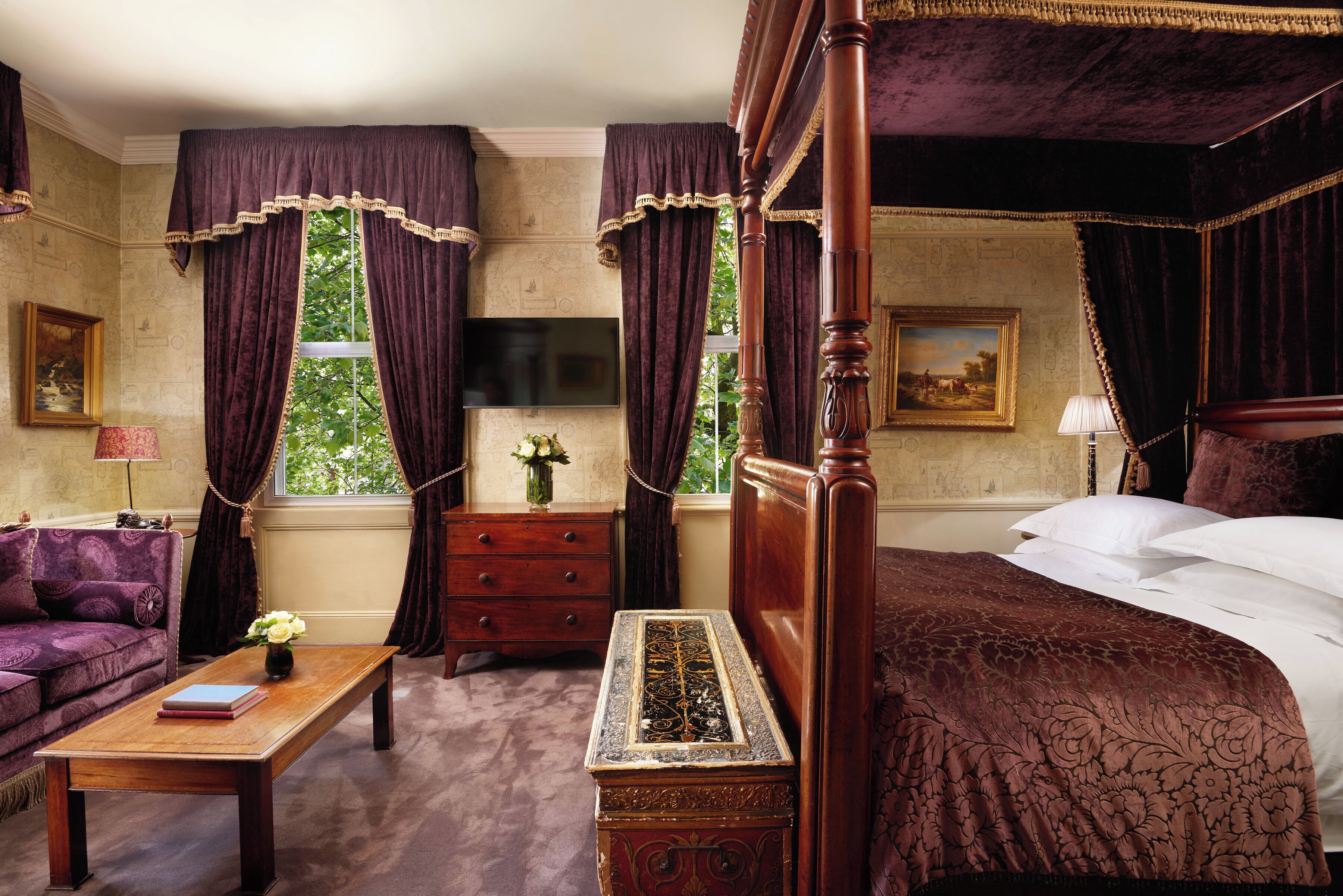 A bedroom with a four-poster bed, a wooden nightstand, a dresser, a sofa, and a television.