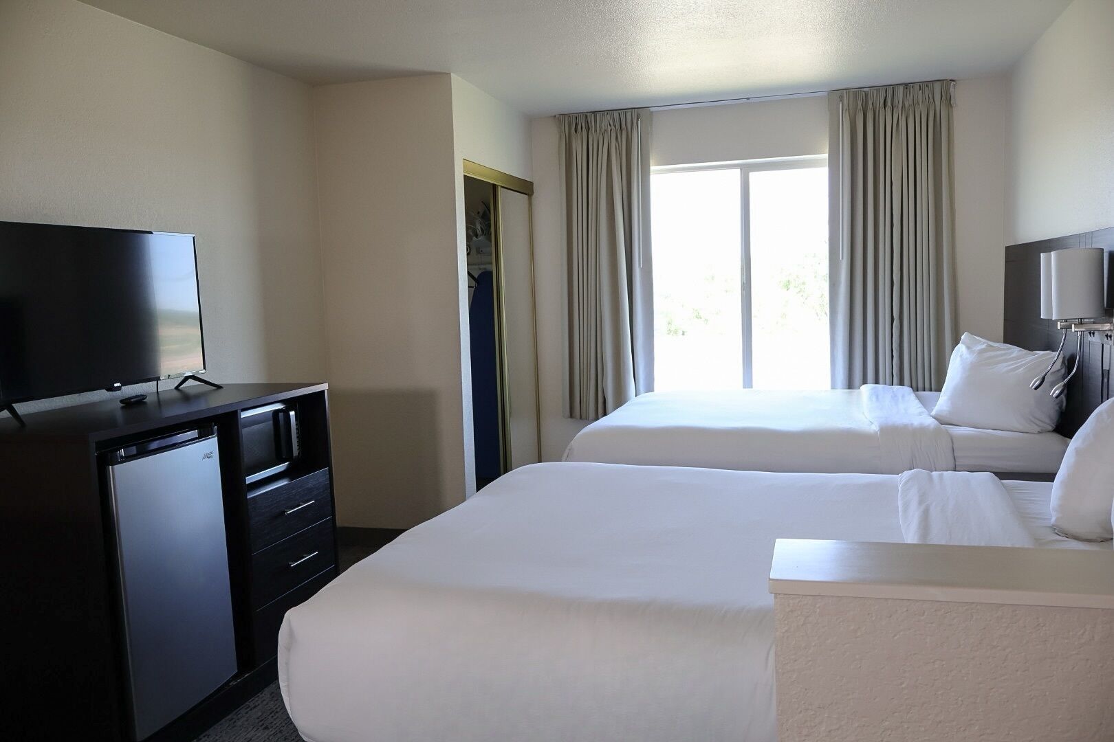 Een hotelkamer met twee bedden, een televisie, een minibar en een groot raam met gordijnen.