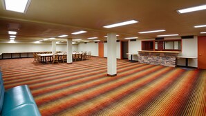 Un salón amplio con alfombra, mesas, sillas, una pared de piedra decorativa y una puerta.