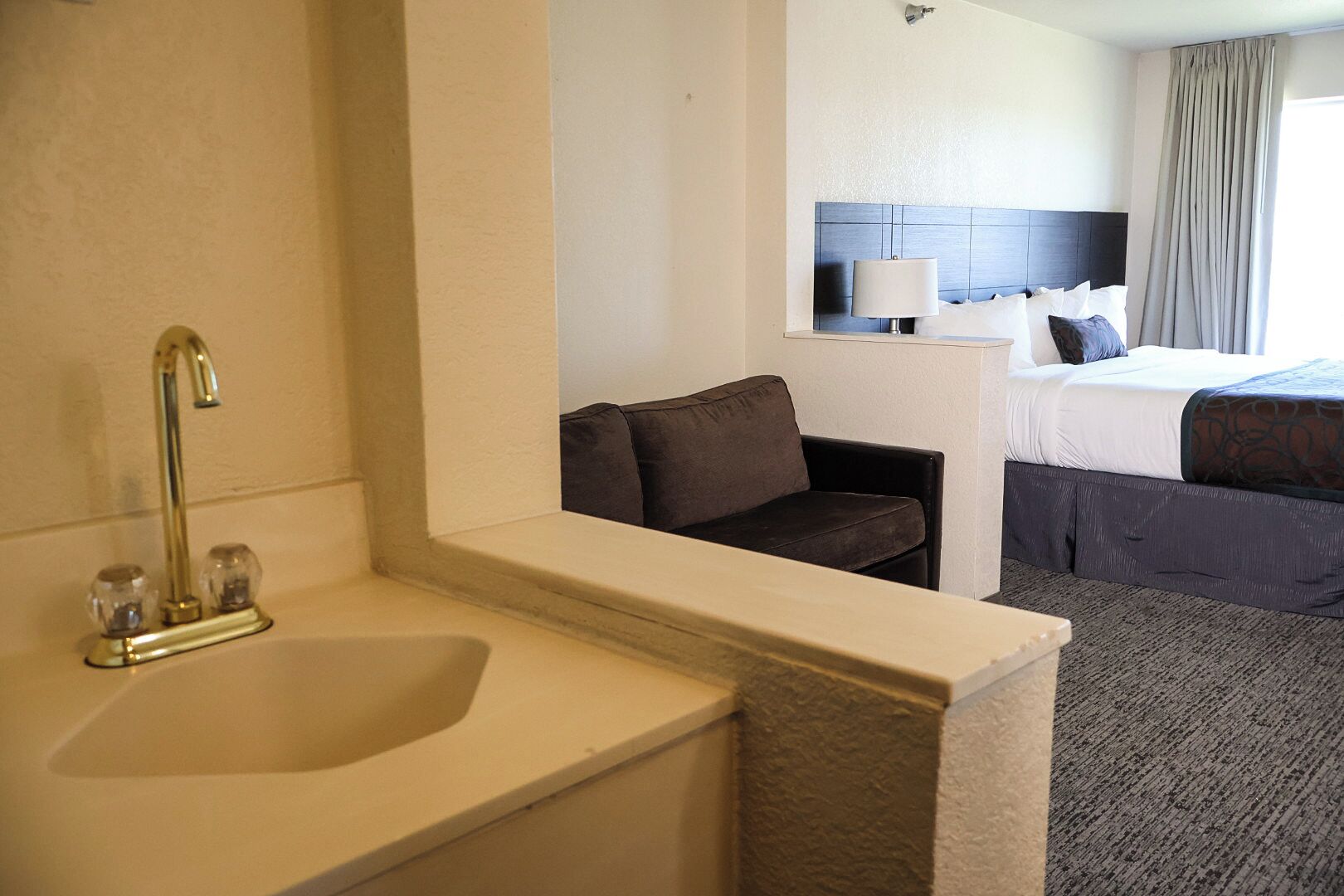 A hotel room with a sink, a chair, a bed, and a nightstand.