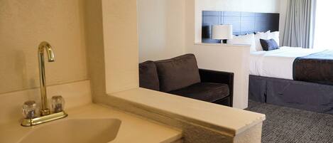 A hotel room with a sink, a chair, a bed, and a nightstand.