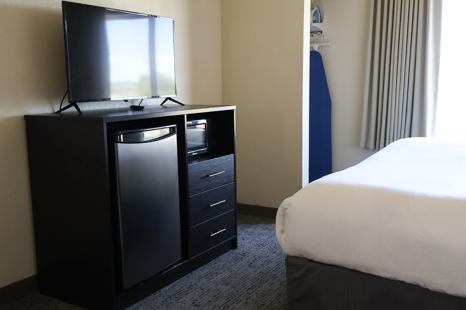 Een hotelkamer met een bed, een zwarte minibars kastje, een televisie en een raam met gordijnen.