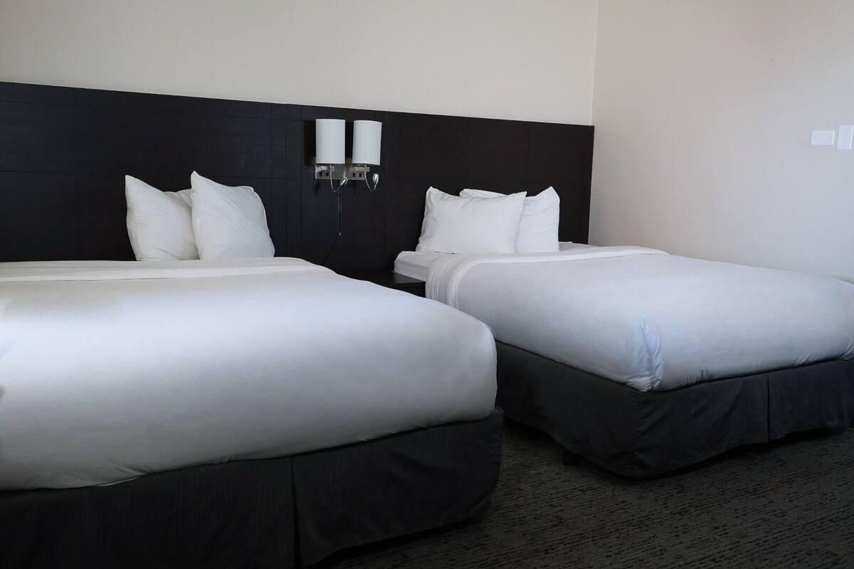 Hotellihuone, jossa on kaksi erillistä sänkyä, tummat päätylevyt, valkoiset vuodevaatteet ja seinään kiinnitetty valaisin.