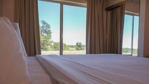 Habitación de hotel con una cama grande, cortinas color beige y vistas a un paisaje por la ventana.