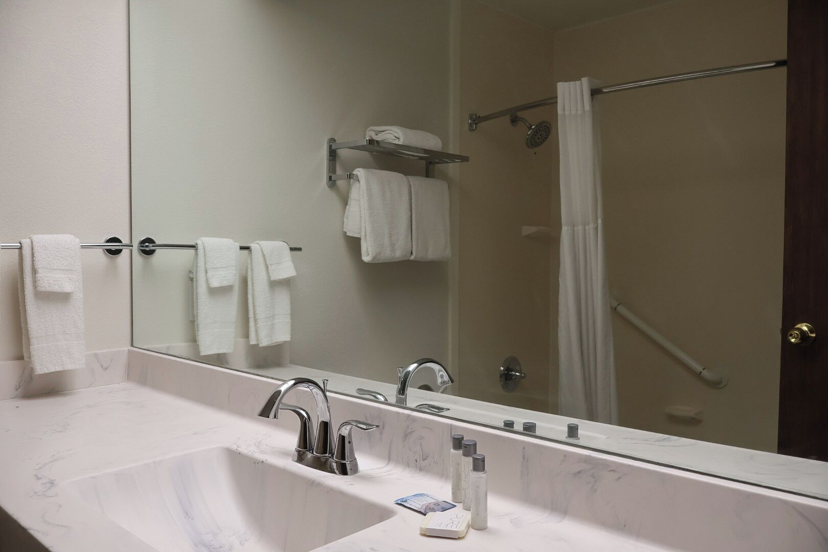 A bathroom with a large mirror, a sink with chrome fixtures, and a shower area.