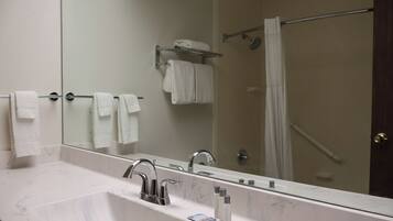 A bathroom with a large mirror, a sink with chrome fixtures, and a shower area.