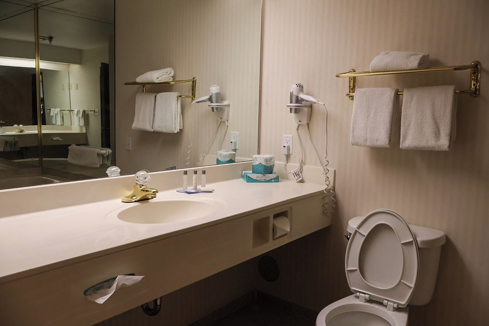 A modern bathroom with a long sink, a gold faucet, a toilet, and a towel rack with towels.