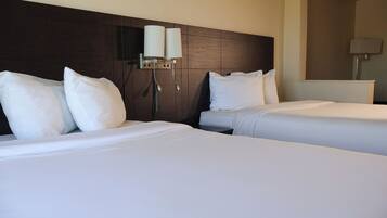 A hotel room with two beds, each with white linens and pillows, a dark wooden headboard, and a wall-mounted lamp.