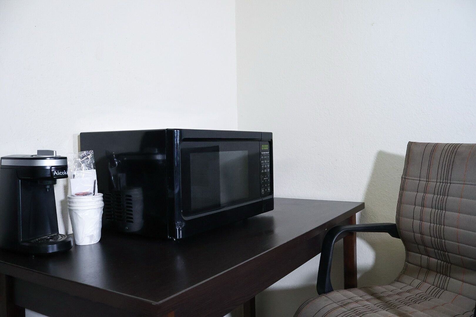 Un forno a microonde su un tavolo, con una macchina da caffè e una tazza.