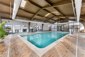 An indoor swimming pool with a brick floor, large windows, and a high ceiling with exposed beams.