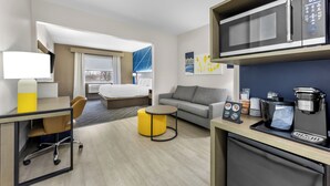 Ett hotellrum med en säng, en soffa, ett skrivbord med en stol, en kaffemaskin och en mikrovågsugn.