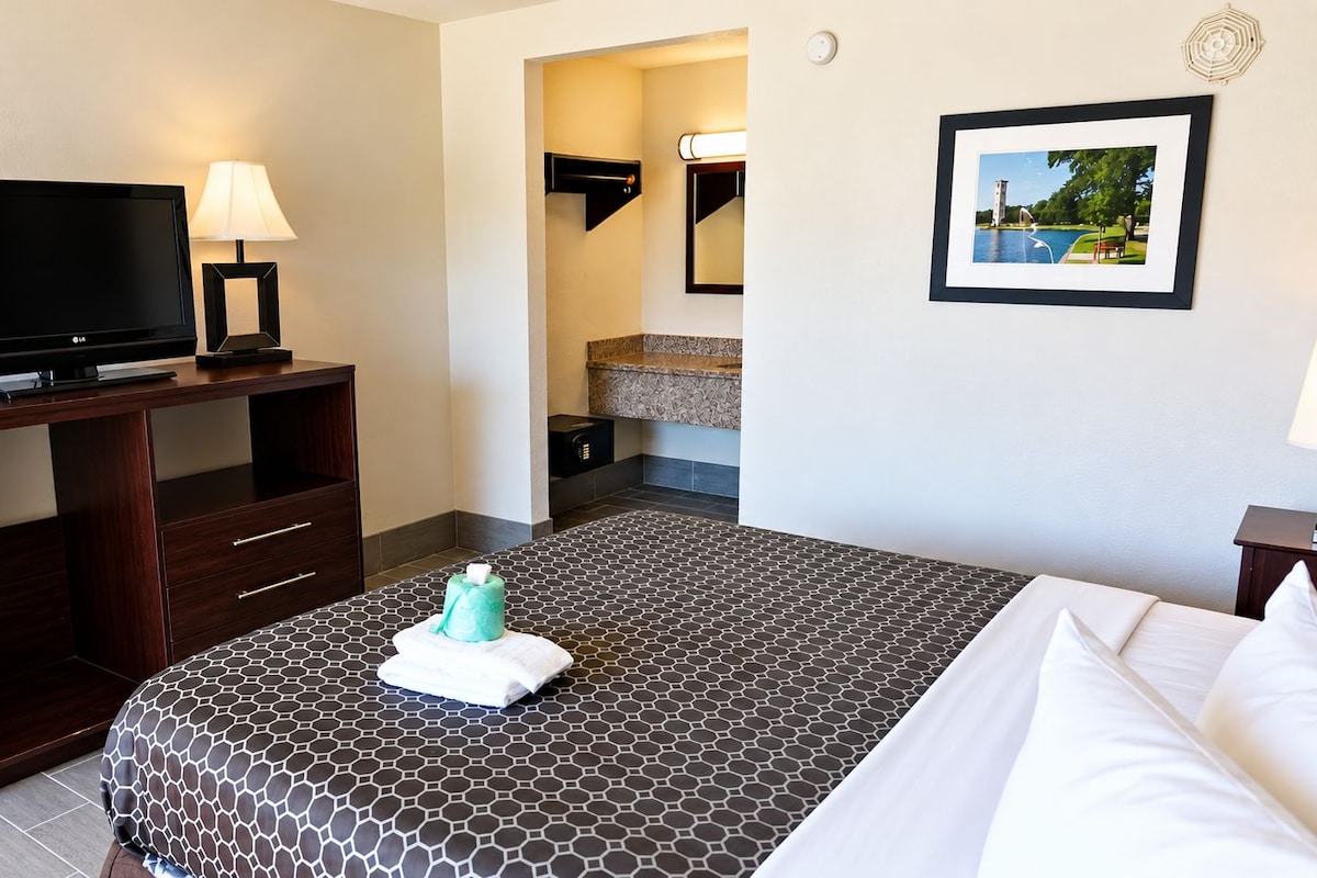 A hotel room with a bed, a desk with a TV, a bathroom, and a framed picture on the wall.