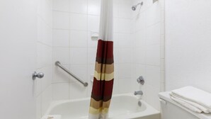 A bathroom with a bathtub, a shower curtain, a toilet, and a handrail.