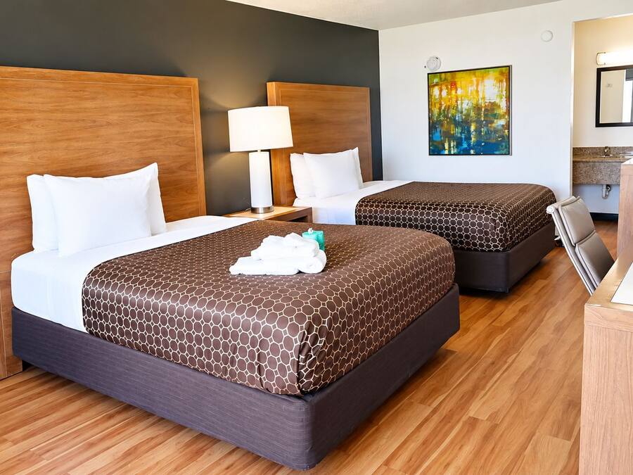 Habitación de hotel con dos camas, un escritorio, una silla, una lámpara y obras de arte en la pared.