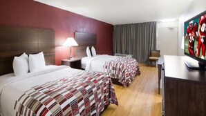 A hotel room with two beds, a desk, a TV, and a lamp.