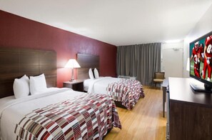 Habitación de hotel con dos camas, un escritorio, un televisor y una lámpara.