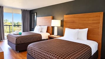 Ein Hotelzimmer mit zwei Betten, einem Nachttisch, einer Lampe und Blick ins Freie.