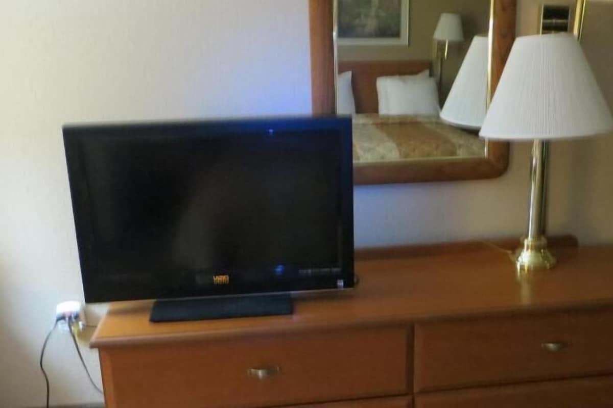 A television on a wooden dresser with a lamp beside it.