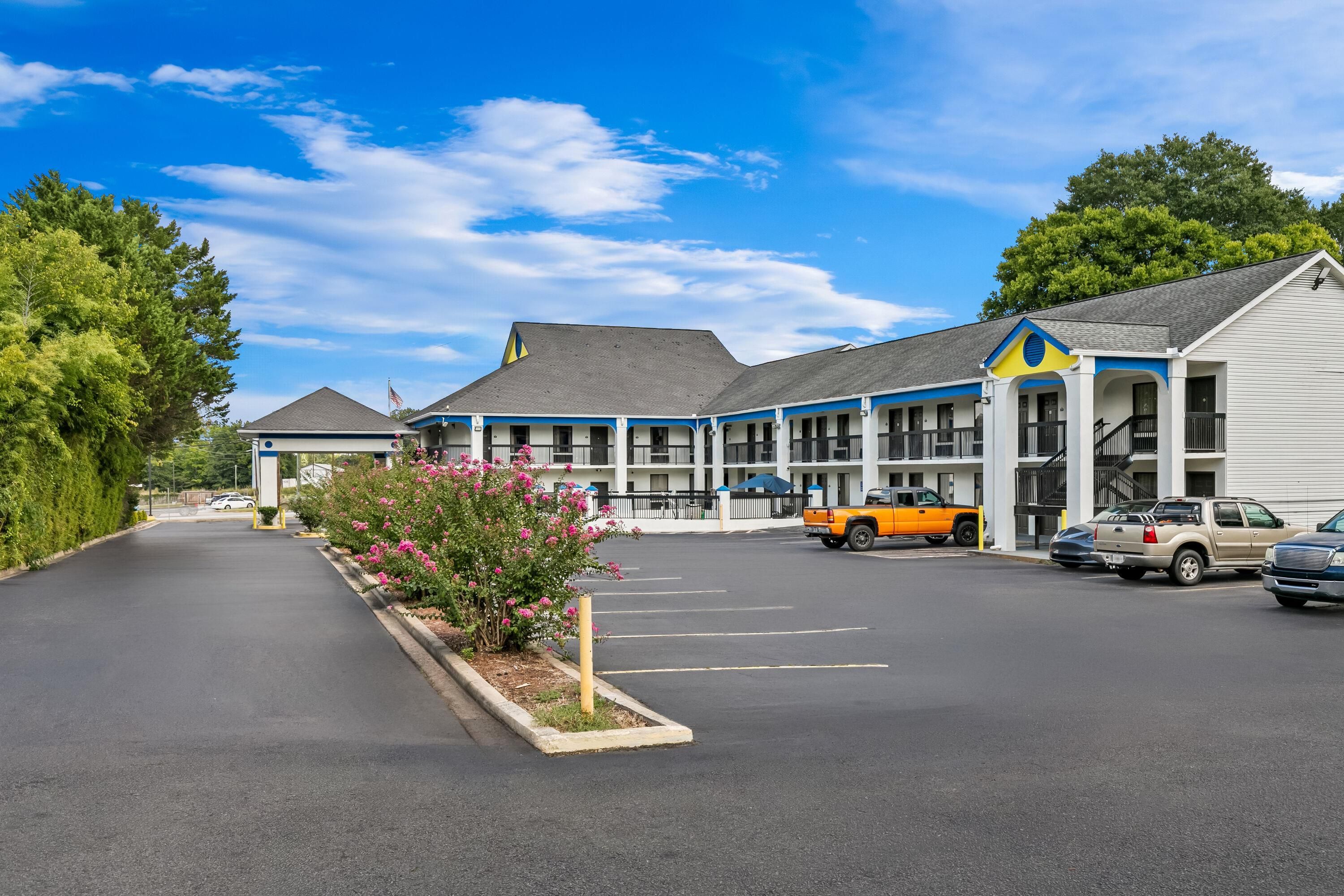 A motel with a parking lot, a yellow truck, and a row of rooms with a blue and white facade.