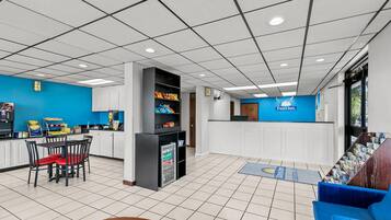 A hotel lobby with a reception desk, seating area, and a kitchenette.