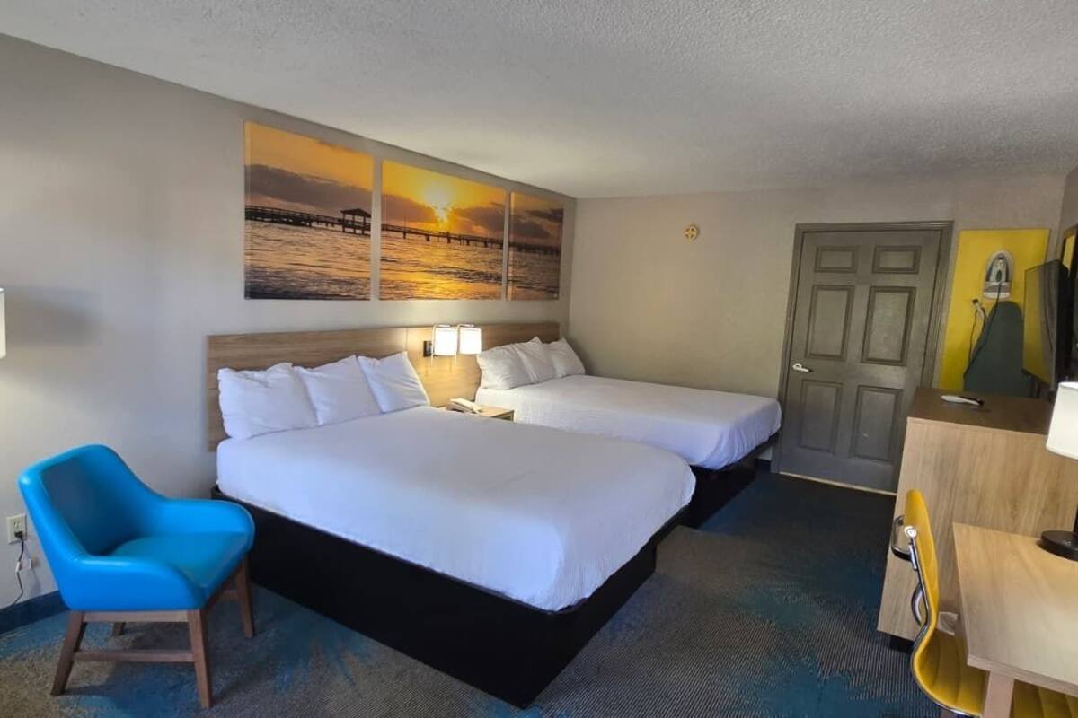 A hotel room with two beds, a desk, a chair, and a large window.