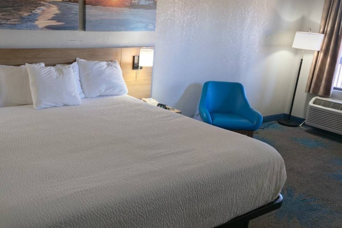 A hotel room with a large bed, a blue armchair, a nightstand, and wall-mounted lamps.