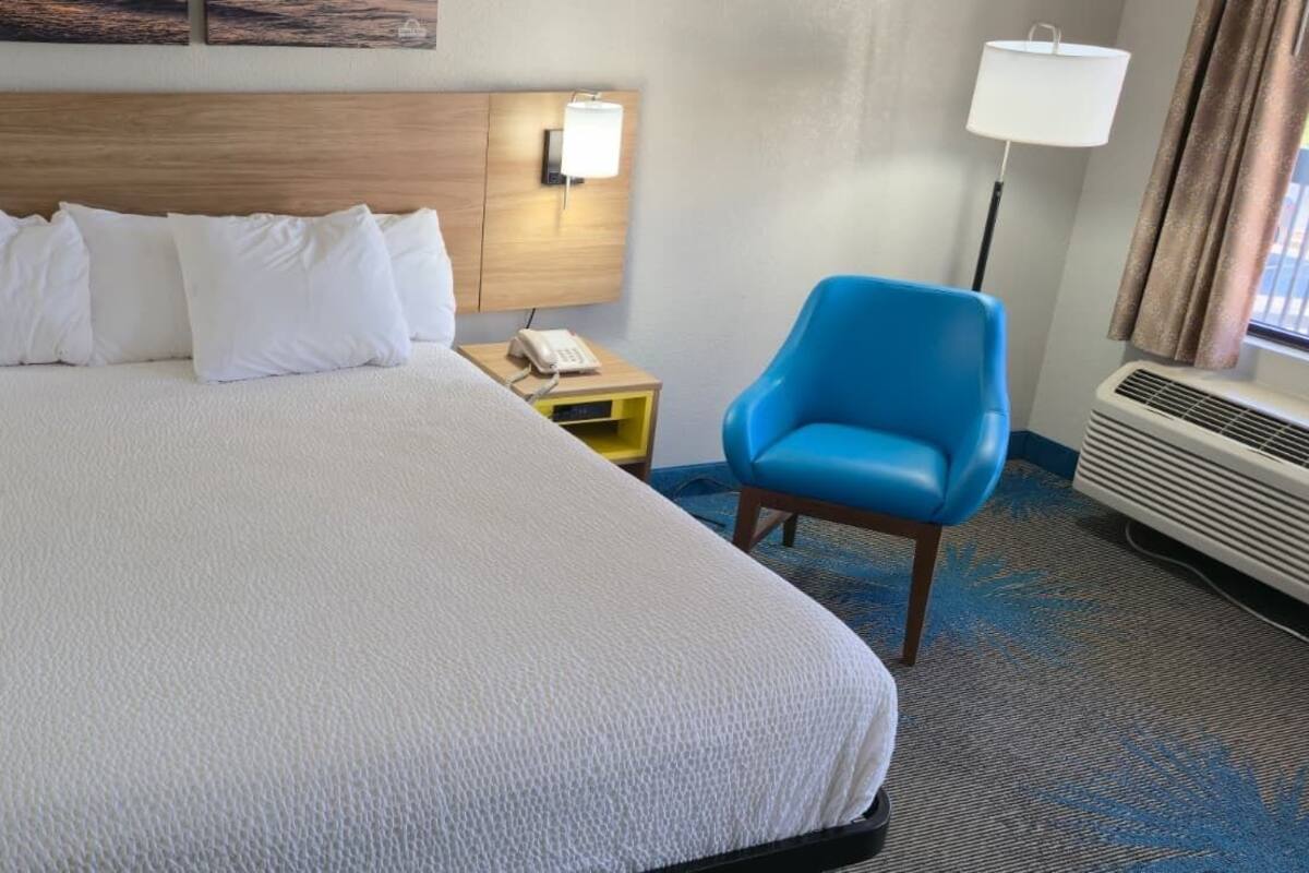 A hotel room with a large bed, two bedside tables, a blue armchair, and a wall-mounted lamp.