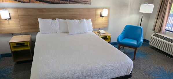 A hotel room with a large bed, two bedside tables, a blue armchair, and a wall-mounted lamp. - Days Inn by Wyndham Elberton (Elberton)