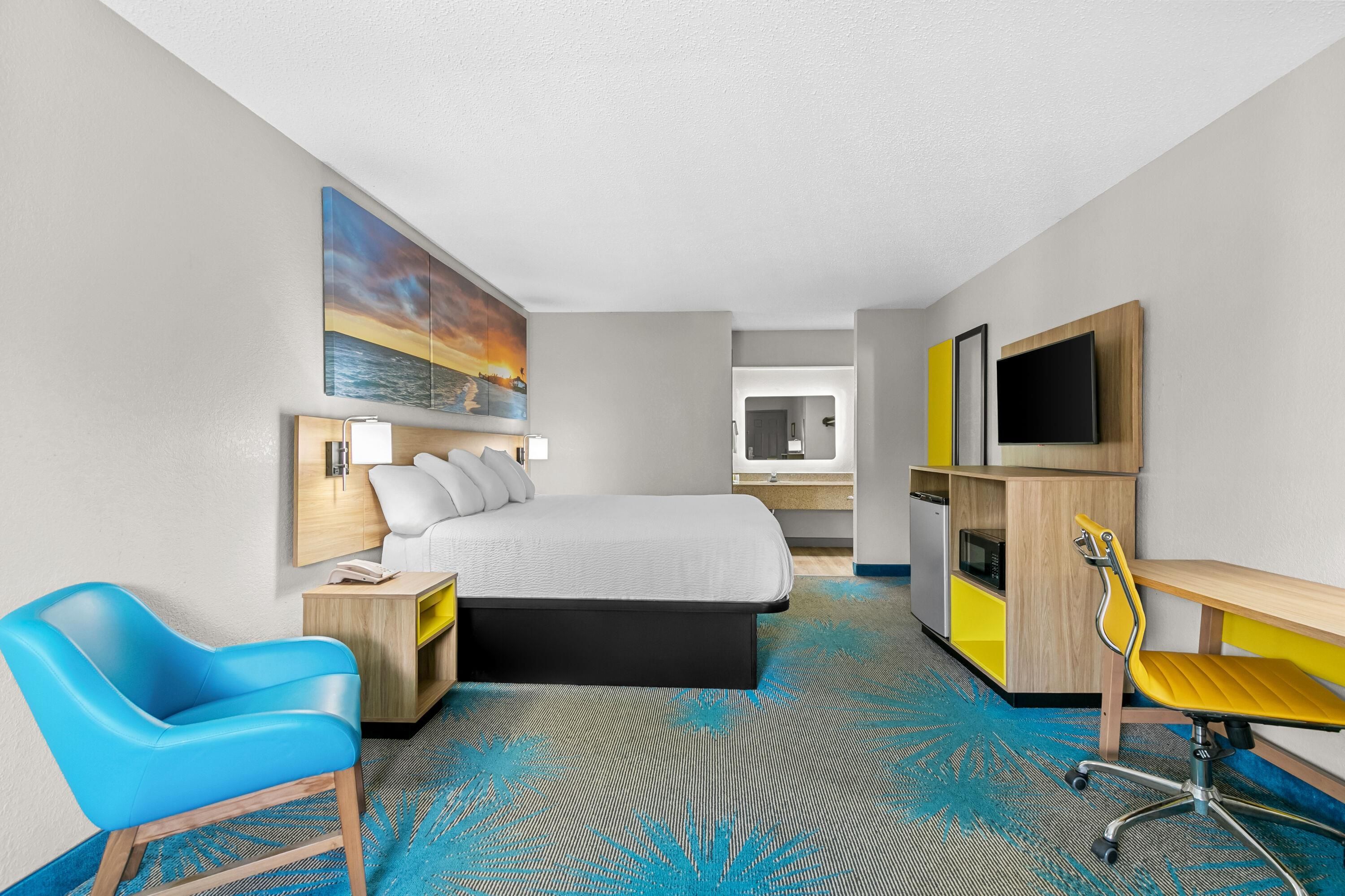 Une chambre d’hôtel avec un lit, un bureau, une chaise, une télévision et un tableau au mur.
