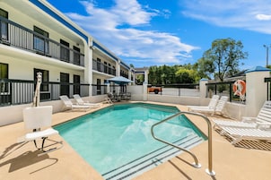 A hotel pool area with a clear blue pool, sun loungers, and a covered seating area.