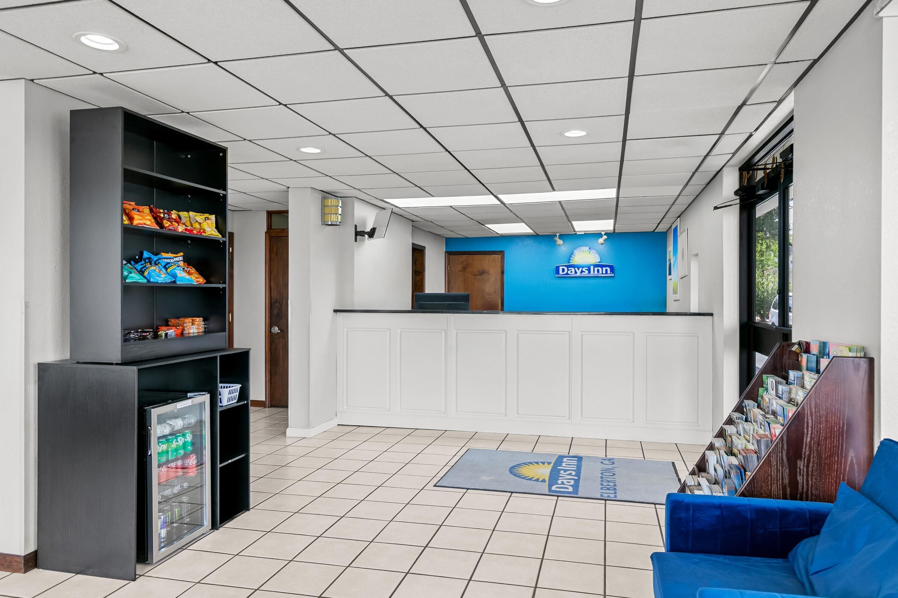 A reception area with a blue counter, a refrigerator stocked with beverages, and a blue couch.