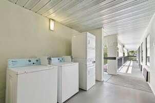 A laundry area with Whirlpool washers and dryers, a ceiling with a perforated design, and a corridor with windows.