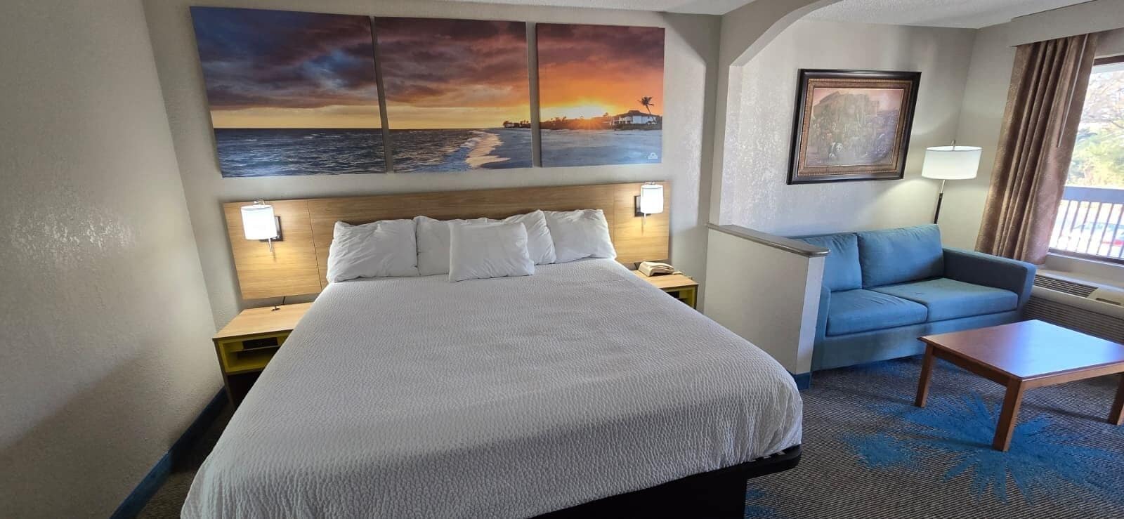 Ein Hotelzimmer mit einem großen Bett, einer Couch, einem Couchtisch und Kunstwerken an den Wänden.