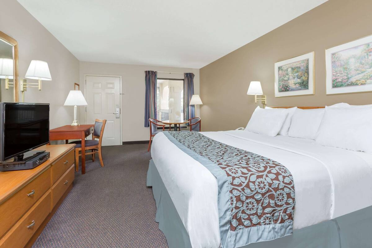 A hotel room with a bed, a desk with a chair, a television, and two lamps.