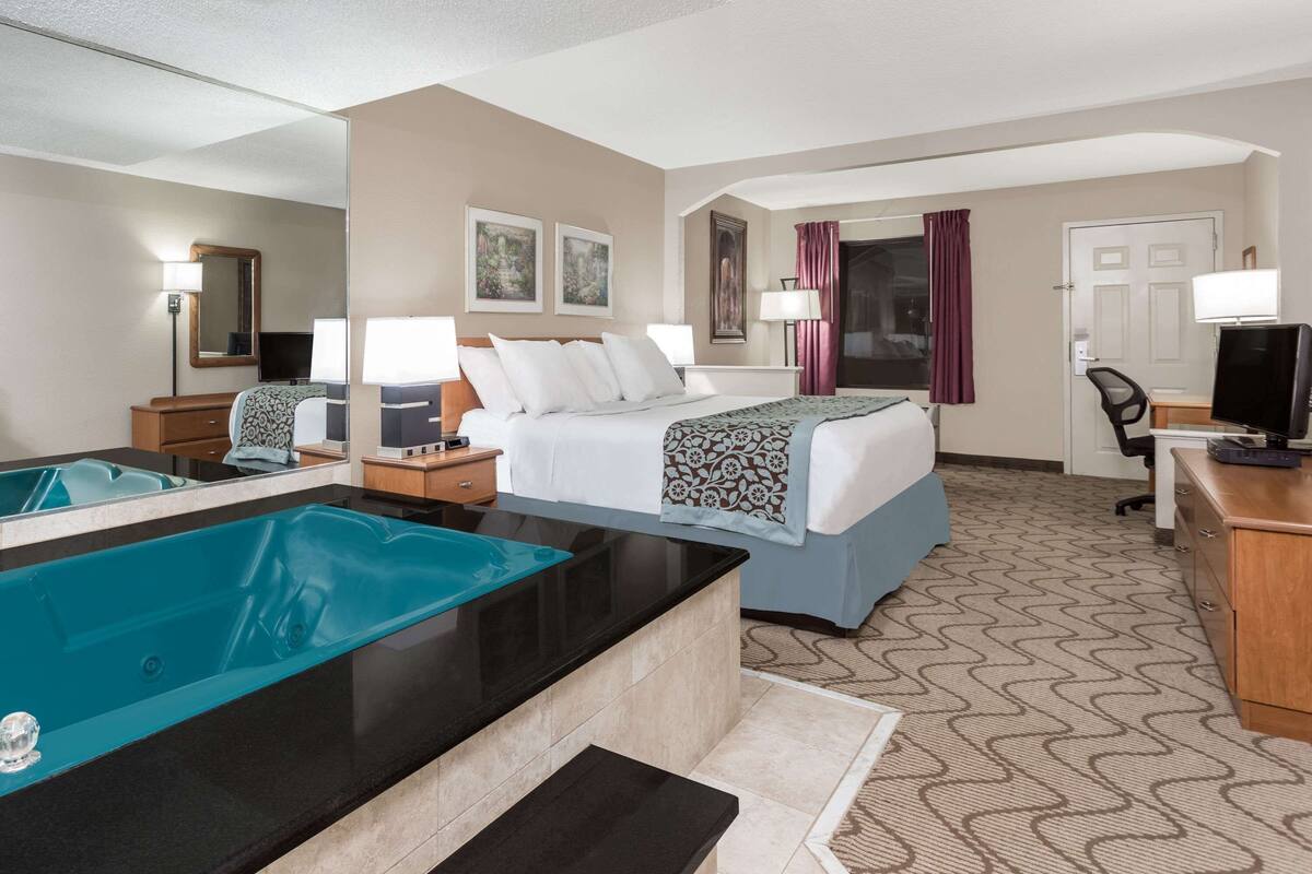 A hotel room with a bed, a desk, a chair, a TV, a mirror, and a bathtub.