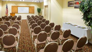A conference room with rows of chairs, a podium, a projector screen, and a table with brochures.