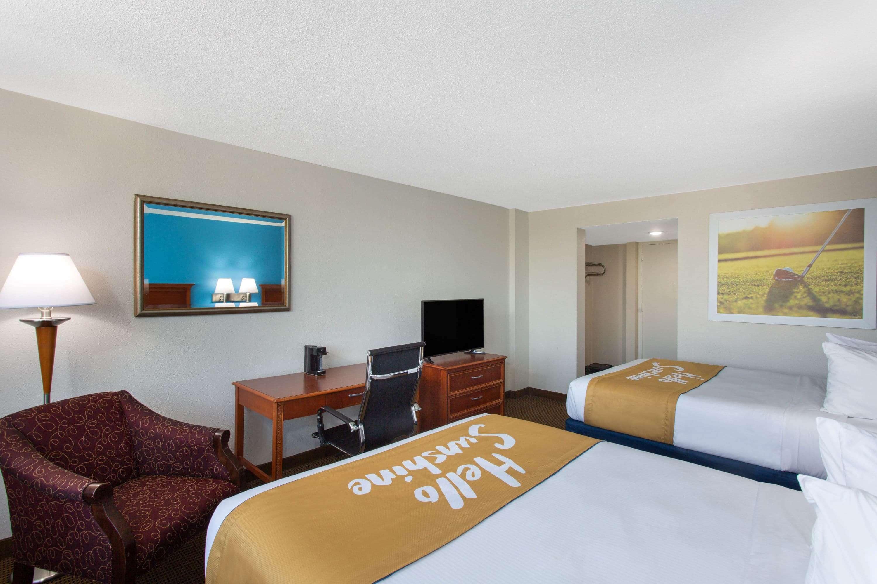 Habitació d'hotel amb dos llits, una taula de treball, una cadira, un televisor i una làmpada.