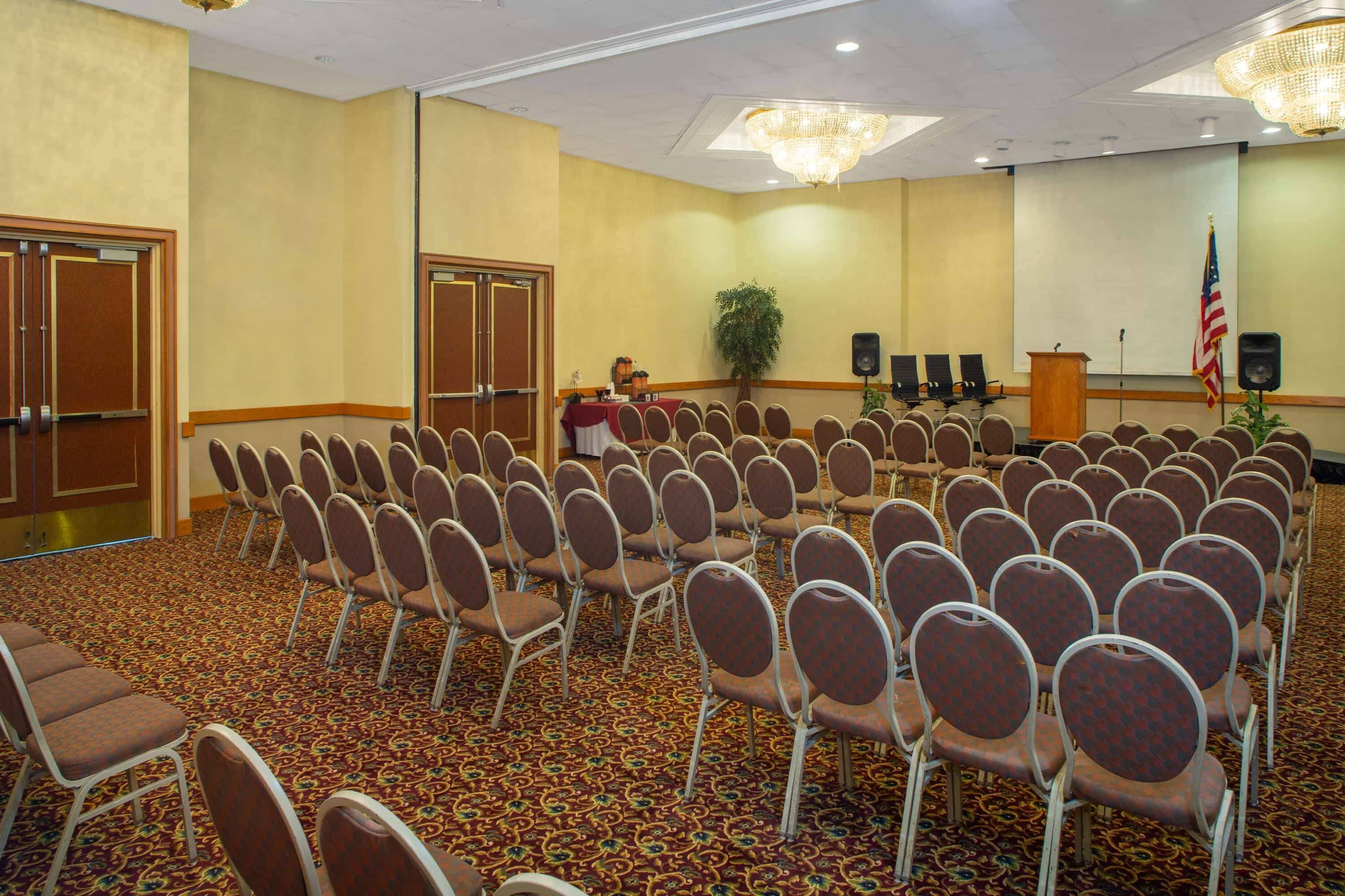 A conference room with rows of chairs, a podium, an American flag, and a speaker.