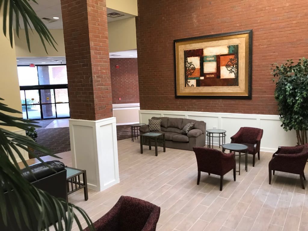 A spacious lobby with a brick wall, a framed abstract painting, a sofa, and several chairs.