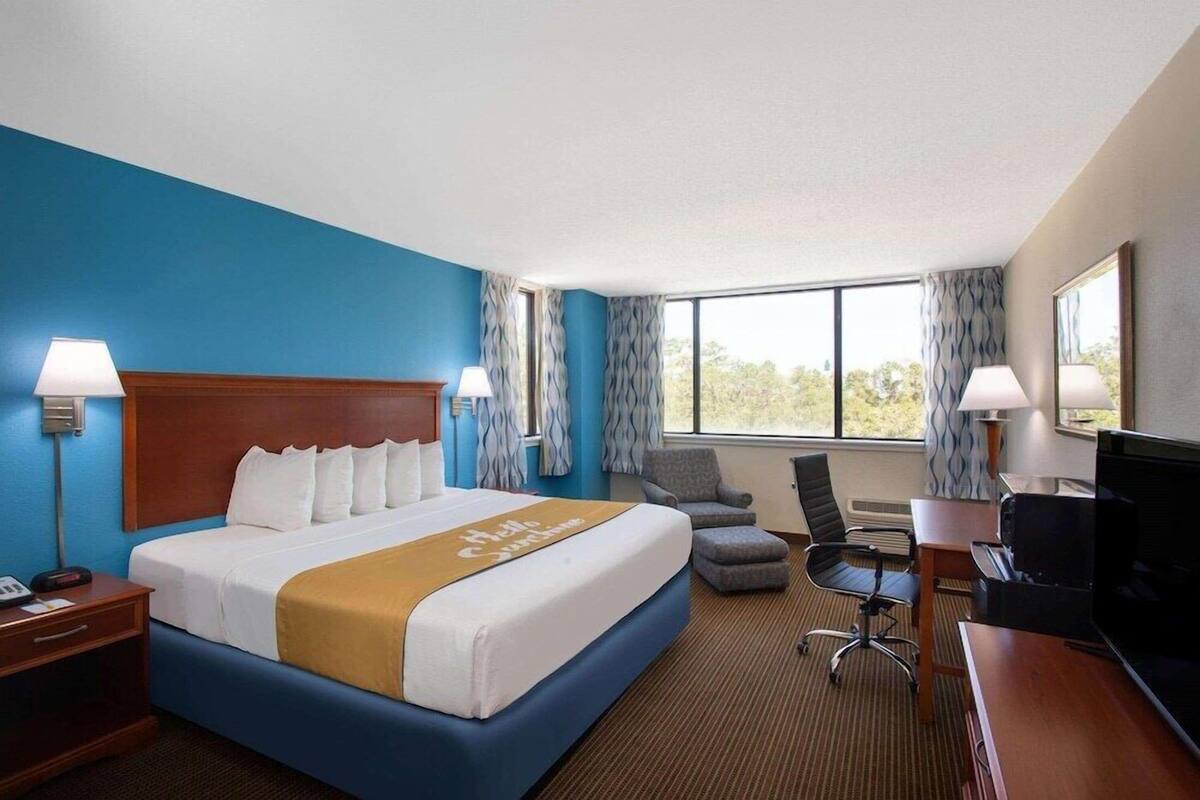 Une chambre d’hôtel avec un grand lit, deux tables de chevet, un bureau avec une chaise, une télévision et une fenêtre avec des rideaux.