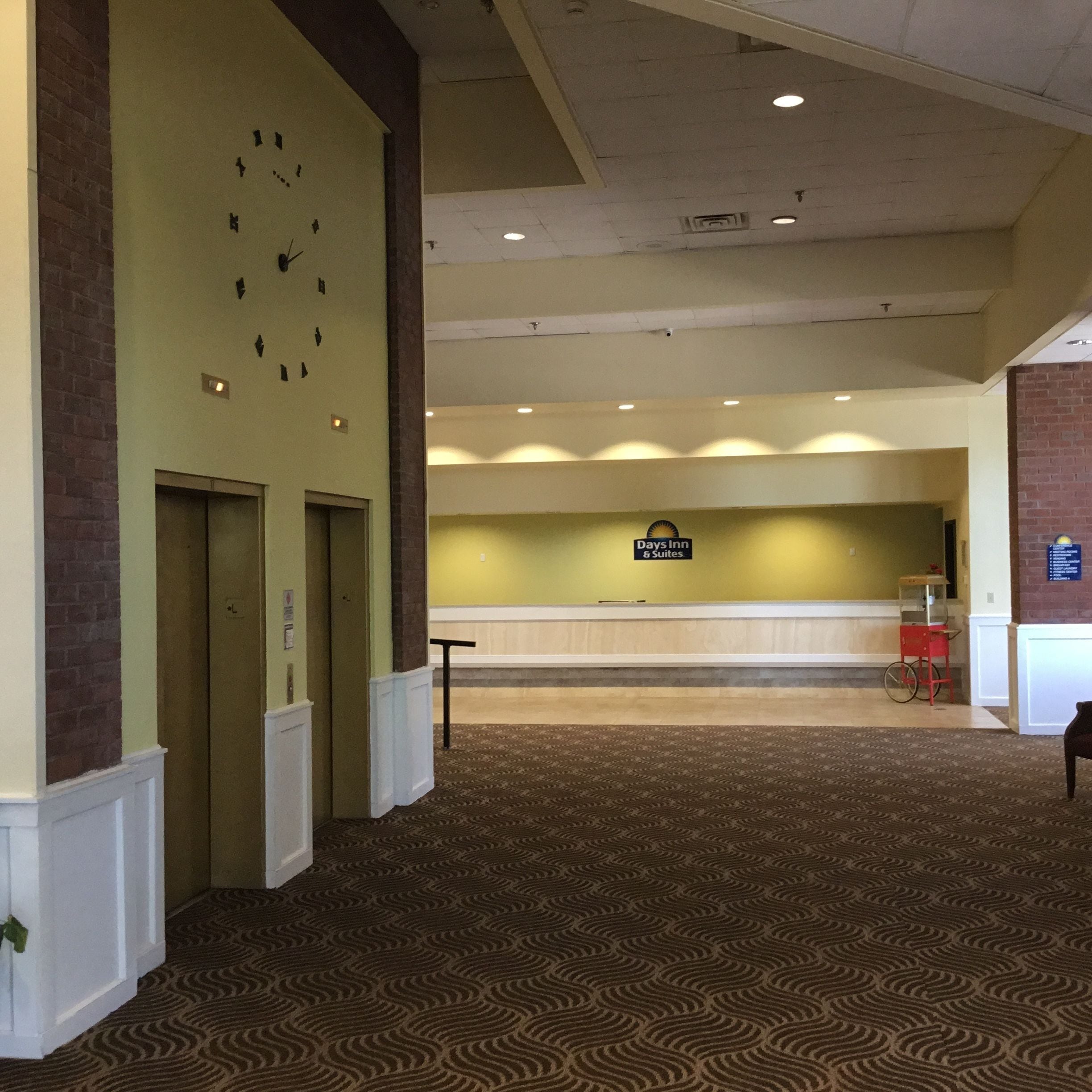 A hotel lobby with a reception desk, a clock on the wall, and a red cart.