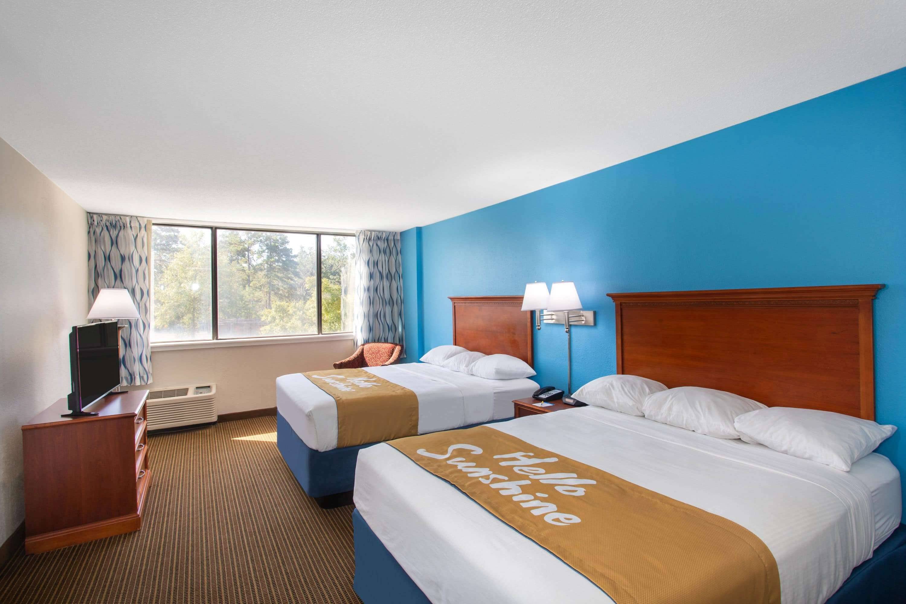 Une chambre d’hôtel avec deux lits, une télévision, un bureau et une fenêtre avec des rideaux.
