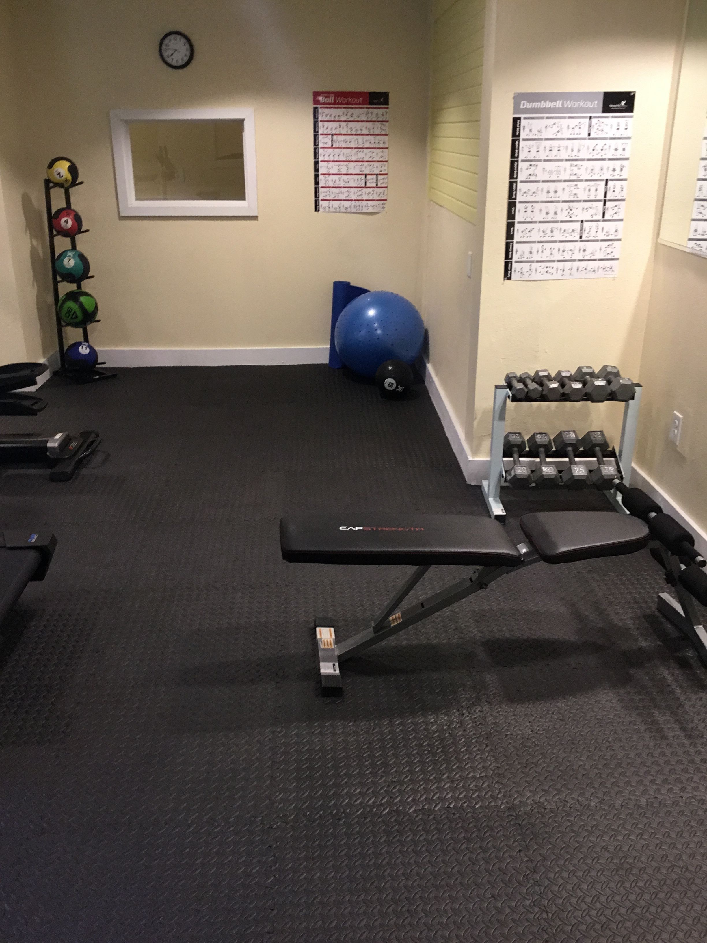 A gym with exercise equipment, a bench, a wall clock, and a window.