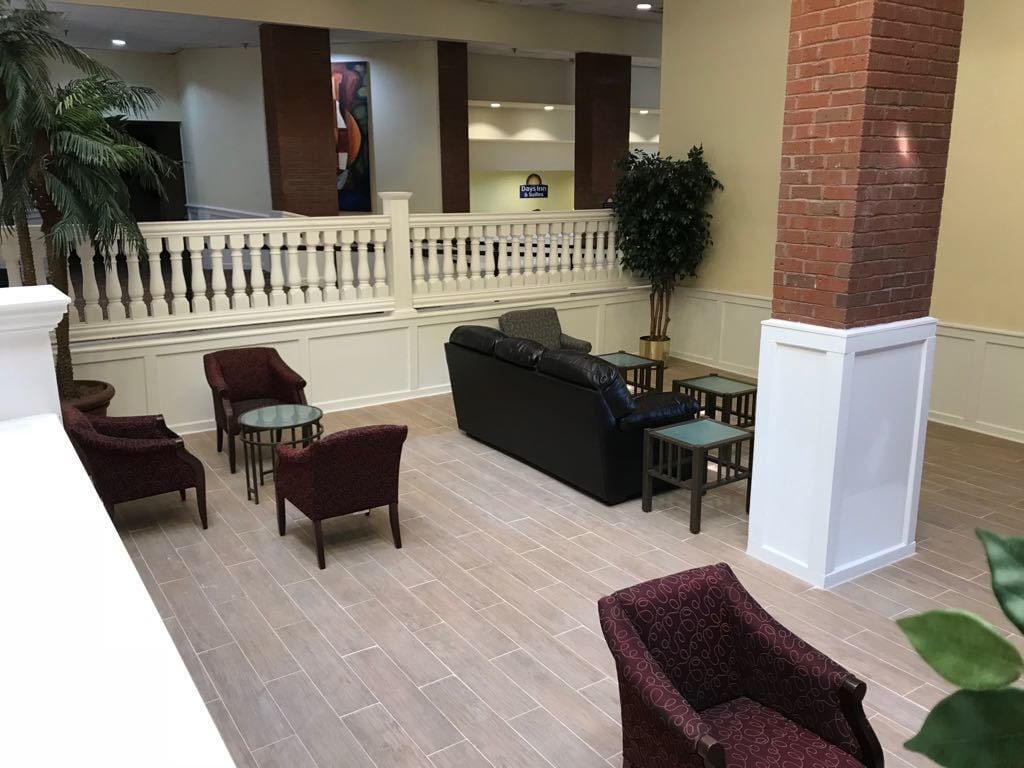 A lobby with a black sofa, red armchairs, a glass table, and a brick pillar.