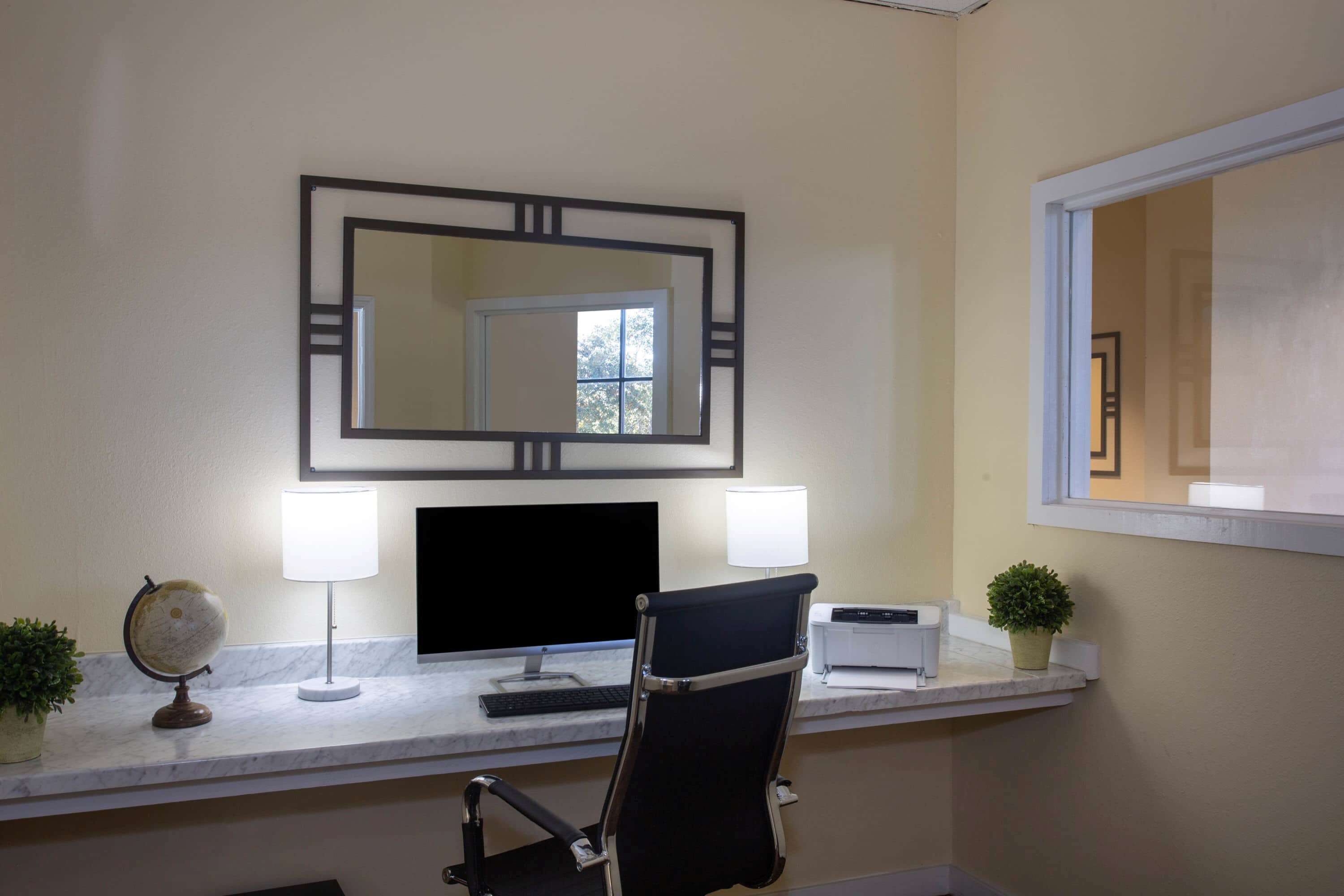 A hotel room with a desk, two lamps, a globe, a printer, and a potted plant.